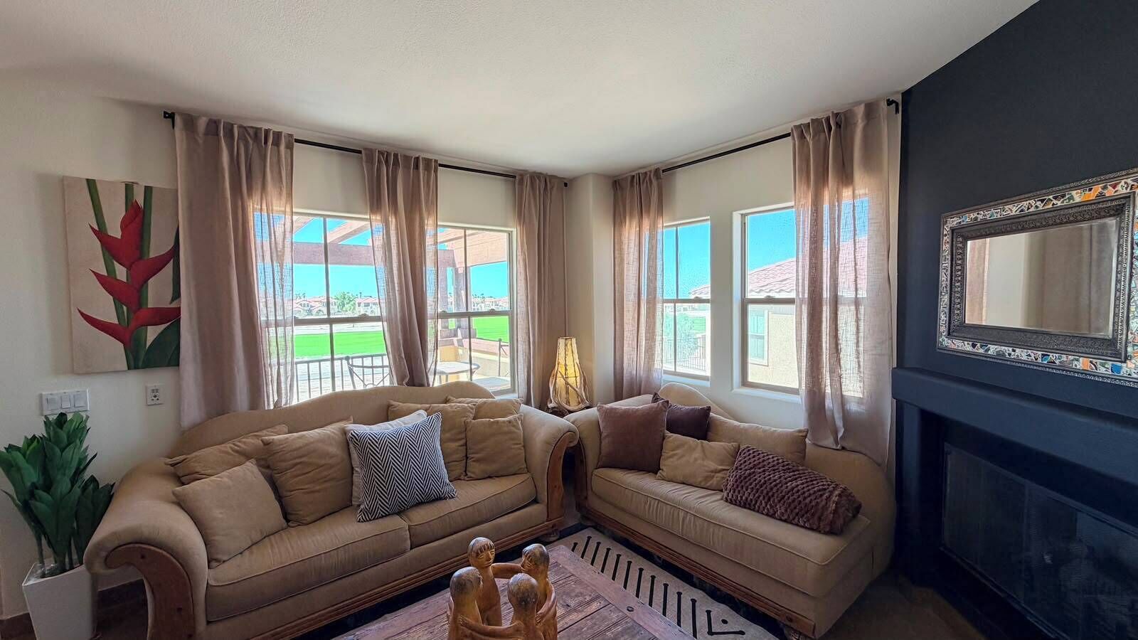 A living room with two sofas, a fireplace, and large windows with curtains.