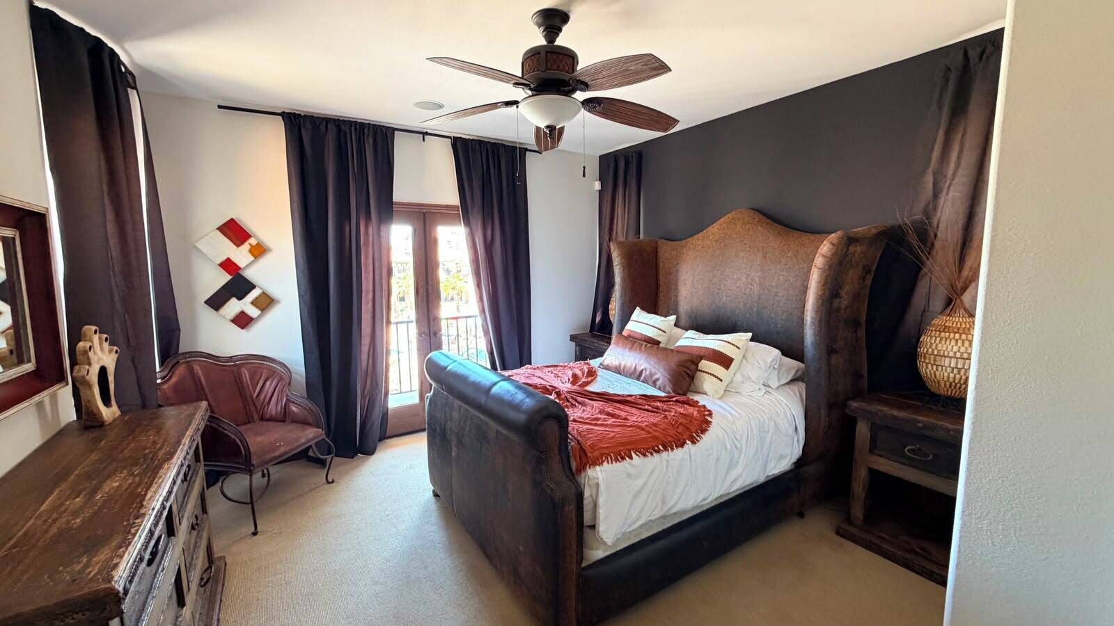 A bedroom with a bed, a desk, a chair, a ceiling fan, and a window with curtains.