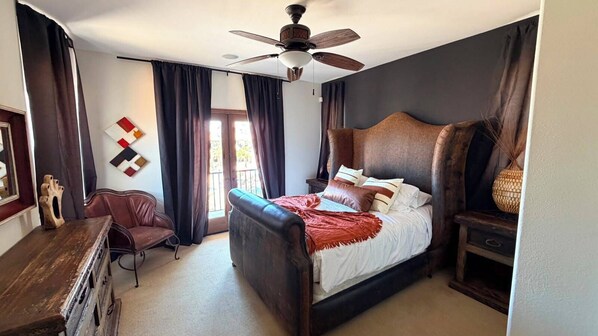 A bedroom with a bed, a desk, a chair, a ceiling fan, and a window with curtains.
