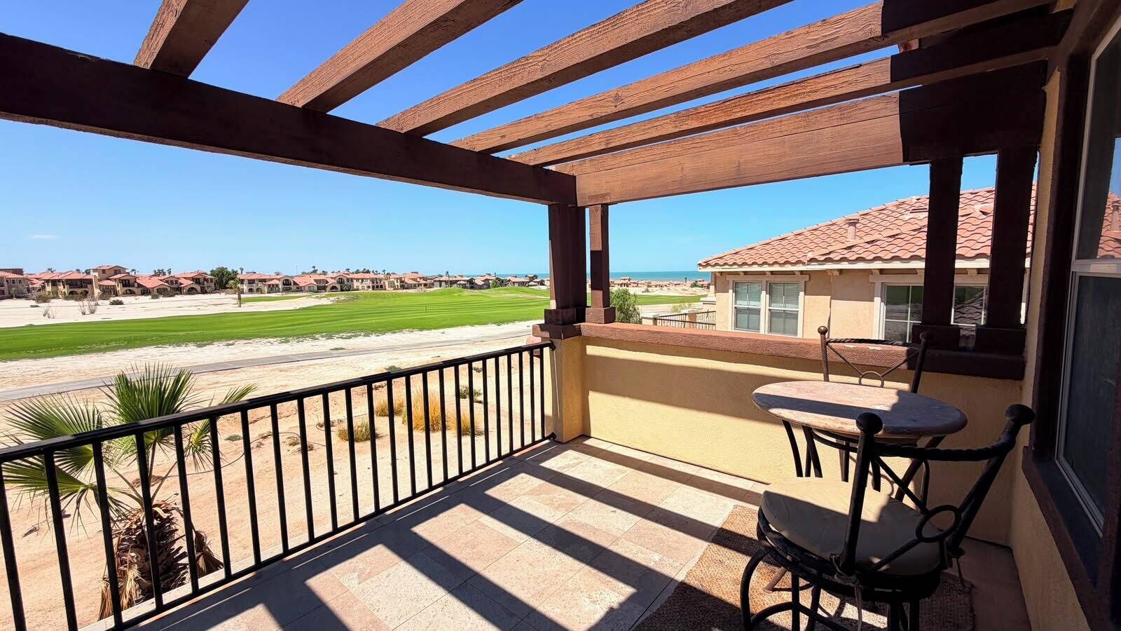 A covered outdoor area with a table and chairs, overlooking a golf course and residential buildings.