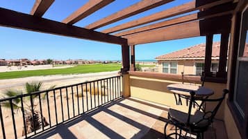 A covered outdoor area with a table and chairs, overlooking a golf course and residential buildings.