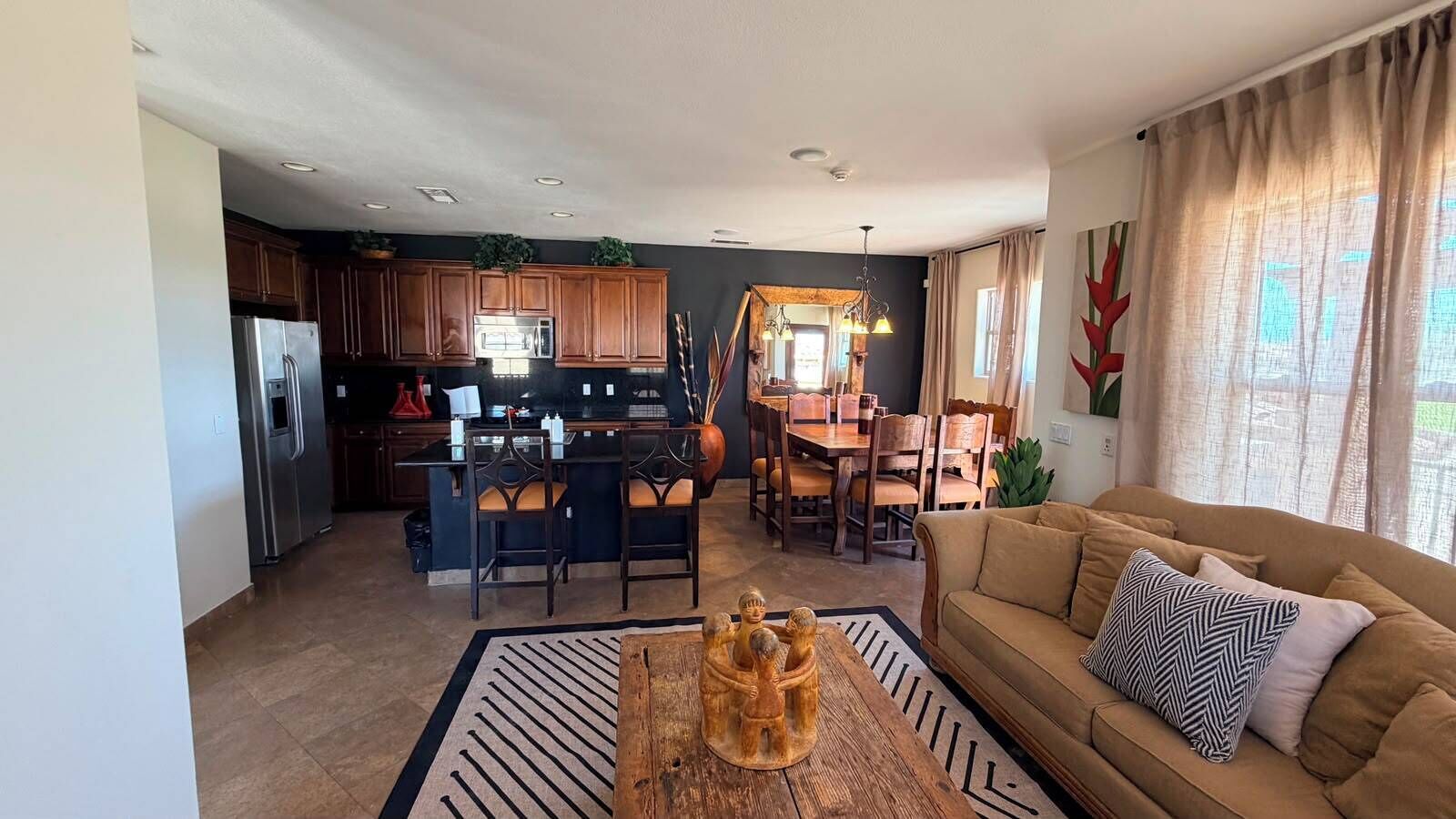 A modern kitchen with dark cabinets, a central island, and a dining area with wooden chairs.