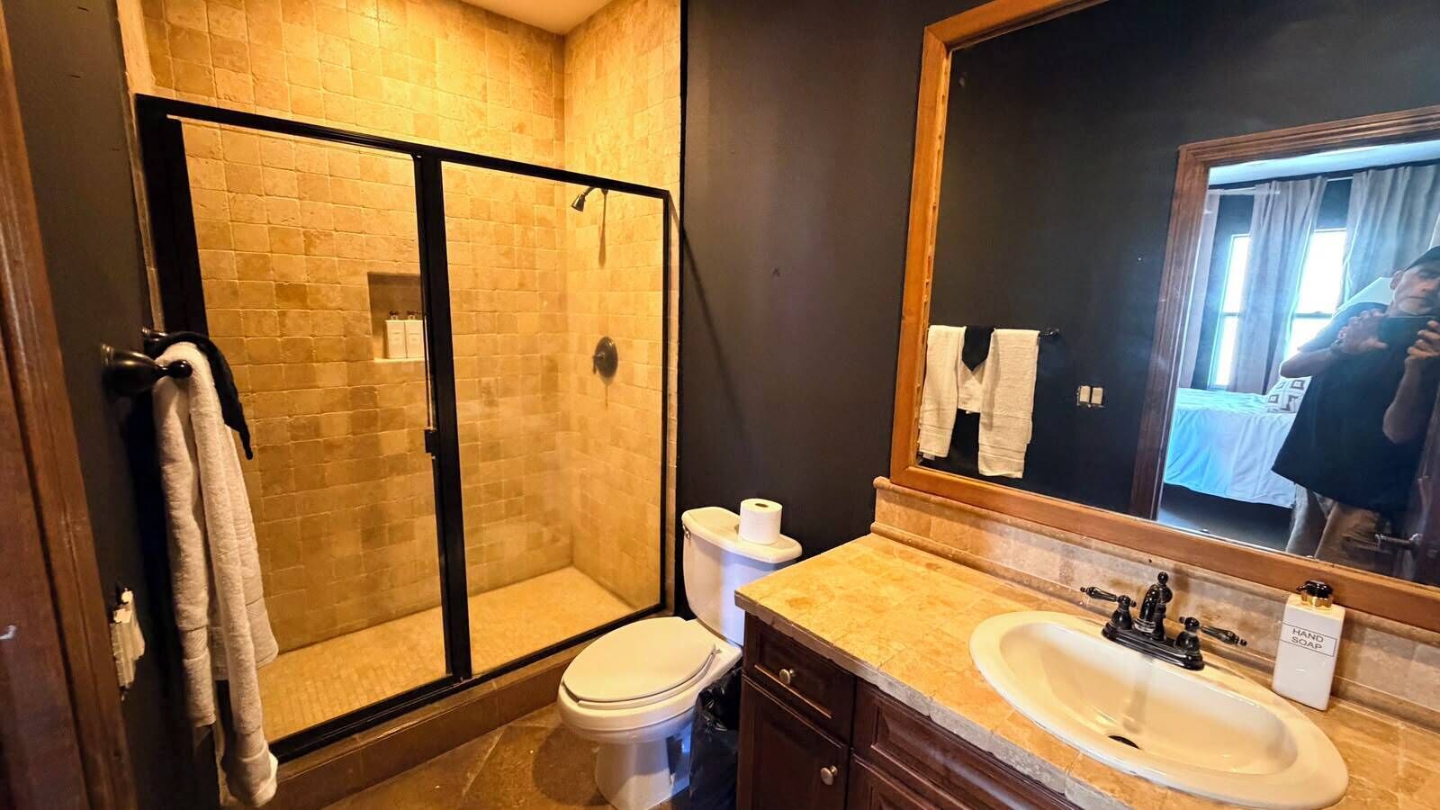 A bathroom with a glass-enclosed shower, a toilet, a sink, and a large mirror.