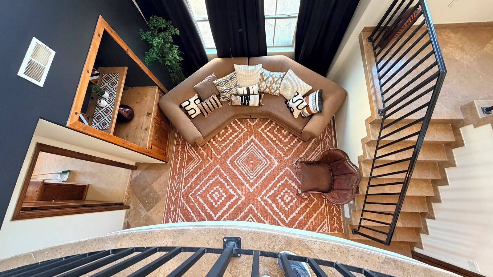 A modern interior with a brown sofa, patterned rug, and a staircase.