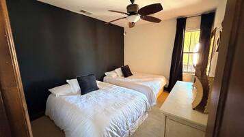 A hotel room with two beds, a ceiling fan, and a window with curtains.