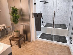 A modern bathroom with a glass shower enclosure, a wooden stool with a potted plant, and a towel rack. - Large Urban Apartment With Steam Sauna 1 (Montreal)