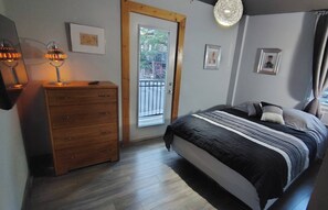 A bedroom with a wooden dresser, a bed with a striped bedspread, and a door leading to an outdoor area. - Large Urban Apartment With Steam Sauna 1 (Montreal)