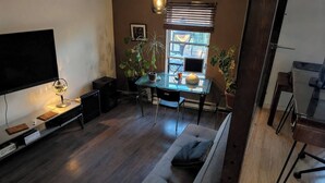 Ett kompakt bostadsutrymme med en platt-TV, ett skrivbord i glas, en dator och en soffa.