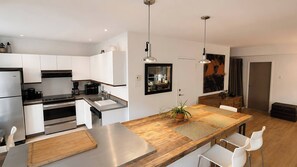 A modern kitchen with stainless steel appliances, a wooden dining table, and white cabinetry. - Large Urban Apartment With Steam Sauna 1 (Montreal)