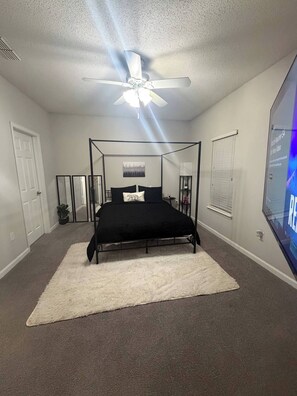 Ein Schlafzimmer mit einem Himmelbett, einem Deckenventilator, einem großen Spiegel und einem an der Wand befestigten Fernseher.
