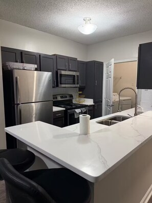 A modern kitchen with dark cabinets, stainless steel appliances, a white marble countertop, and a visible roll of paper towels. - Home away from home (Atlanta)