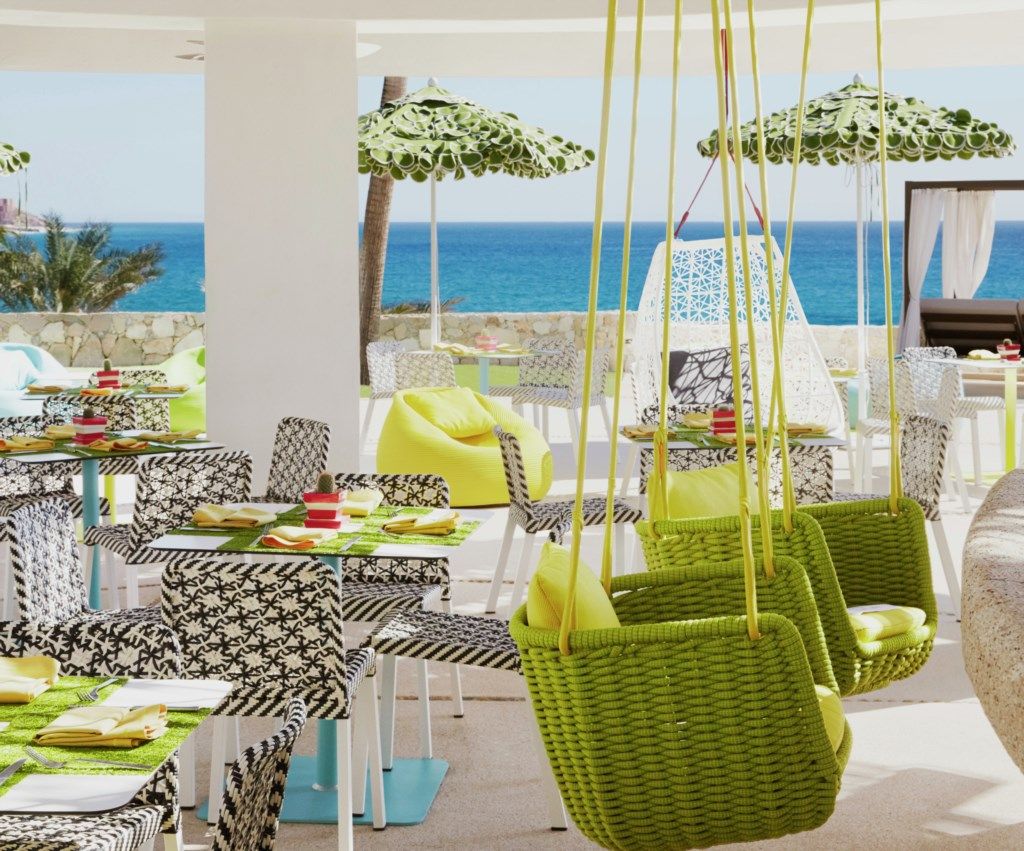 Een terras met tafels en stoelen, hangende groene manden en parasols.