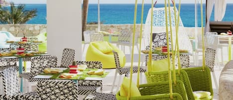 An outdoor dining area with tables and chairs, hanging green baskets, and umbrellas.