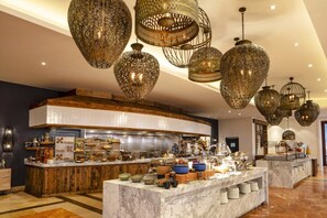 A hotel lobby with a marble reception desk, a curved counter with food and drink items, and ornate hanging light fixtures. - Los Cabos | Elevated Coastal Stay | Pool + Beach (Los Cabos)