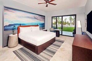 A hotel room with a bed, a painting, a ceiling fan, a TV, a desk, and a view of the outdoors. - Los Cabos | Elevated Coastal Stay | Pool + Beach (Los Cabos)