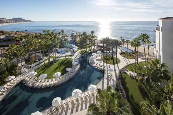 A resort with a large pool, palm trees, and a view of the ocean. - Los Cabos | Elevated Coastal Stay | Pool + Beach (Los Cabos)