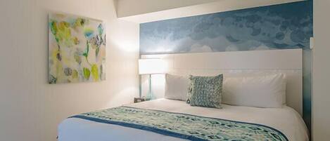 Une chambre d’hôtel avec un grand lit, une tête de lit ornée d’une fresque, une table de chevet avec une lampe et une œuvre d’art accrochée au mur.