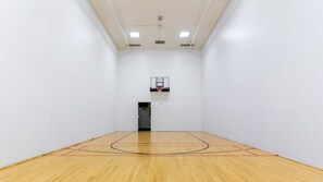 Een sporthal met een basketbalring, houten vloer en witte wanden.