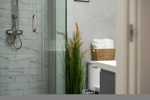 Ein Badezimmer mit Duschkabine aus Glas, einer weißen Toilette und einem Korbwäscher mit Handtüchern.