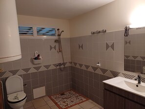 Een badkamer met toilet, wastafel, douche en betegelde wanden.