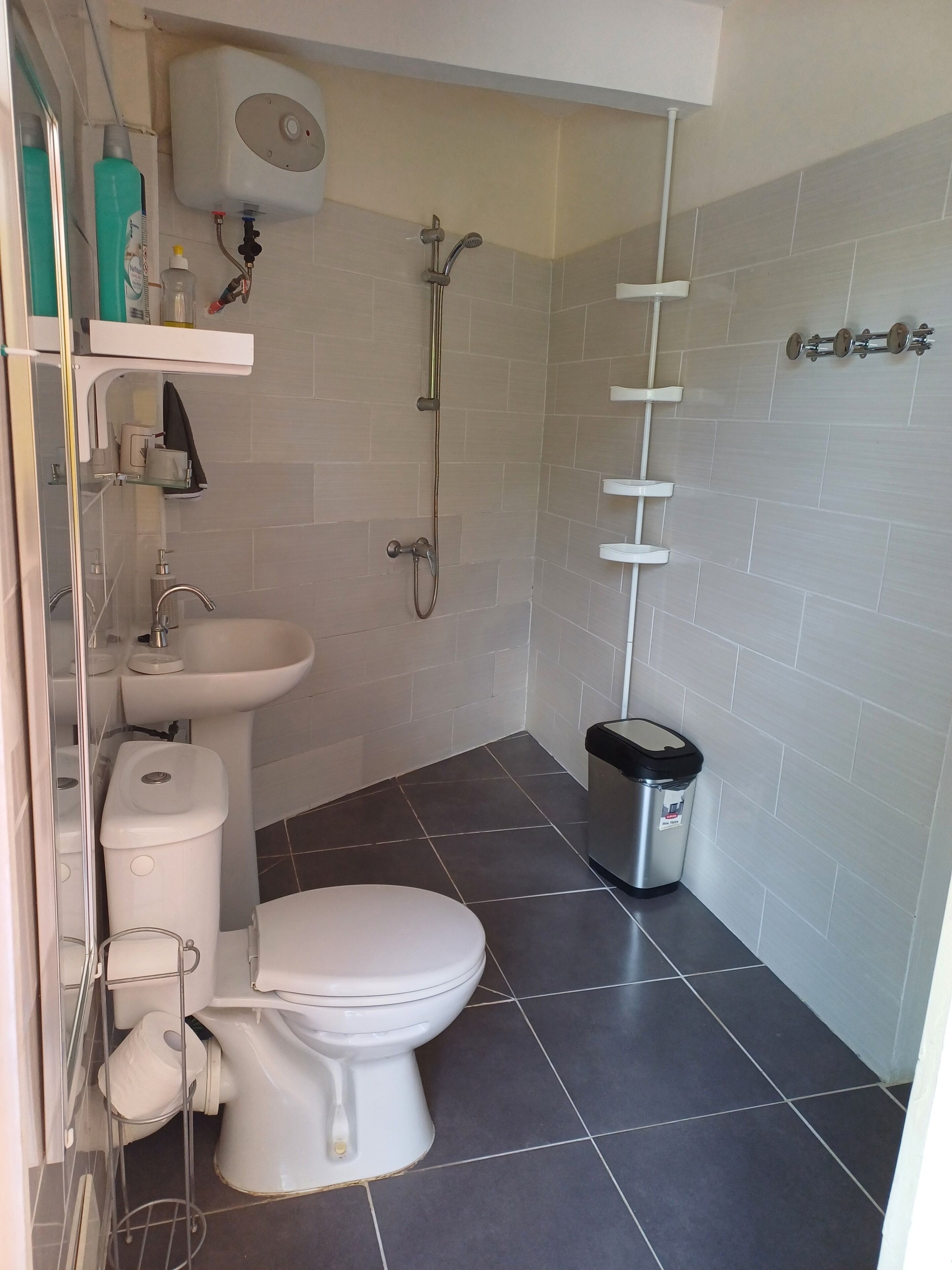 A bathroom with a toilet, sink, shower, and a trash bin.