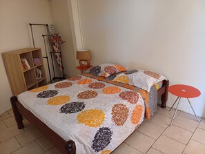 A bedroom with a bed, a wooden wardrobe, a red table, and a lamp. - Nicolas's Shelter (Saint-Esprit)