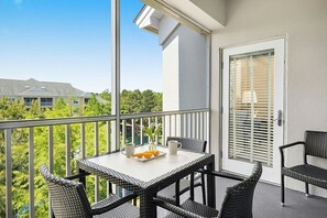 A balcony with wicker furniture, a table with a tray of oranges and a cup, and a door with blinds. - Myrtle Beach | Couples Coastal Retreat | Pool + Hot Tub (Myrtle Beach)