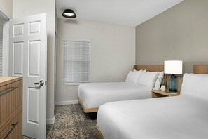 Een hotelkamer met twee bedden, een nachtkastje met een lamp, een raam met zonwering en een deur.