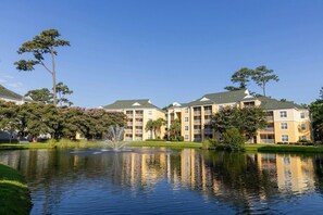 A multi-story hotel with a central courtyard featuring a fountain, surrounded by lush greenery and trees. - Myrtle Beach | Group Beach Retreat | Pool + Hot Tub | 2BR (Myrtle Beach)