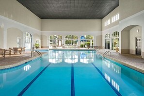 An indoor swimming pool with clear blue water, surrounded by lounge chairs and tables, and large windows allowing natural light. - Myrtle Beach | Group Beach Retreat | Pool + Hot Tub | 2BR (Myrtle Beach)
