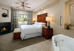 Quarto de hotel com cama, mesa de cabeceira, abajur, lareira, ventilador de teto e banheira.