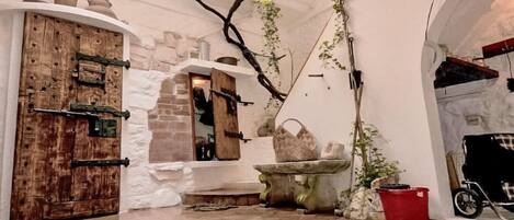 A courtyard with a wooden door, a stone wall, a hanging plant, and a red bucket.