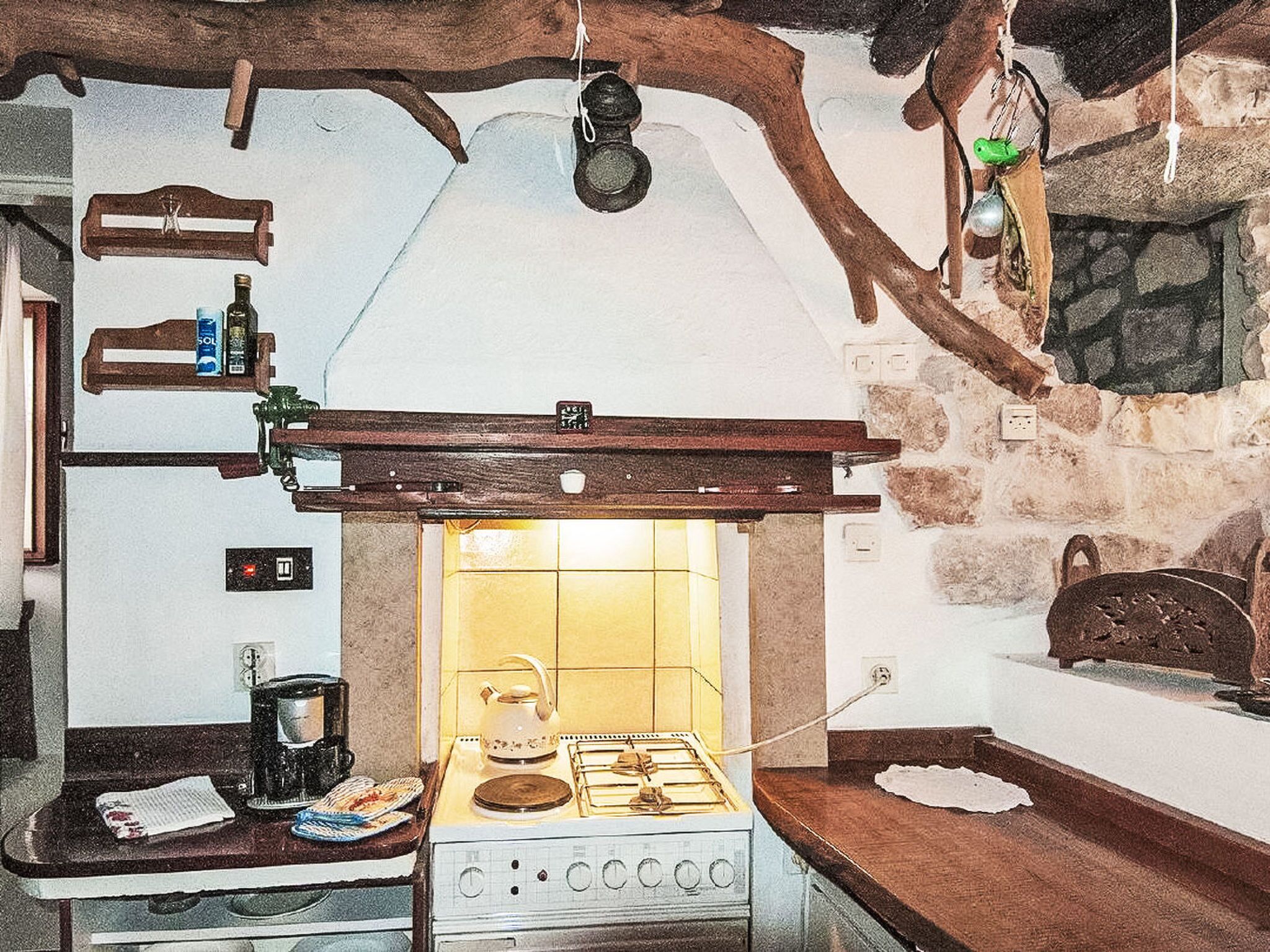 Une cuisine rustique avec un cuisinière à gaz, des poutres en bois et un mur en pierre.