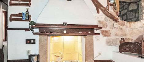 A rustic kitchen with a gas stove, wooden beams, and a stone wall.