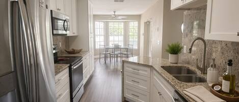 A modern kitchen with stainless steel appliances, white cabinetry, a granite countertop, and a skylight.