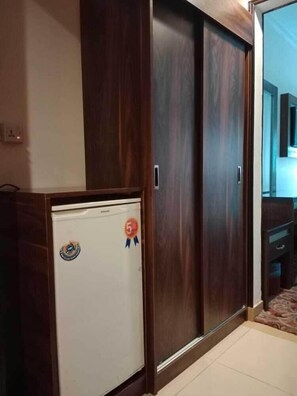 A room with a wardrobe, a small white appliance, and a door leading to another room. - Sky View Hotel (Madinah)