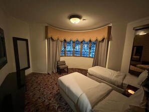A hotel room with two beds, a window with curtains, a small table, and a mirror. - Sky View Hotel (Madinah)