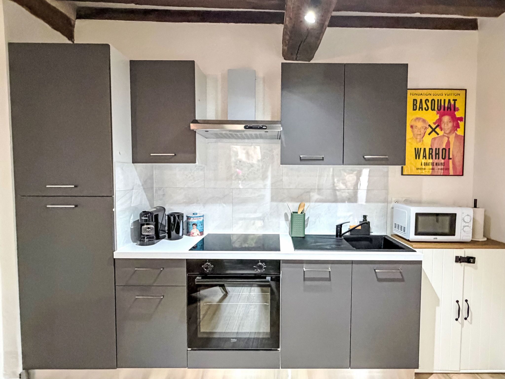 Eine moderne Küche mit grauen Schränken, einem eingebauten Backofen, einer Mikrowelle und einer Kaffeemaschine auf der Arbeitsfläche.