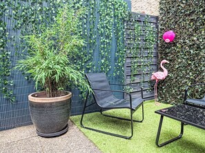 Un espace jardin agrémenté d’une grande plante en pot, d’une chaise en métal noir et d’une statue de flamant rose.