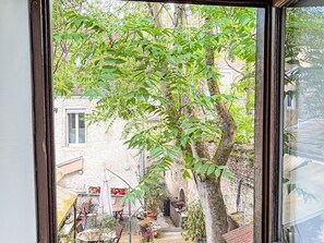 A view through a window of a courtyard with a tree, a building, and outdoor furniture. - Hypercentre Dijon by Interhome (Dijon)