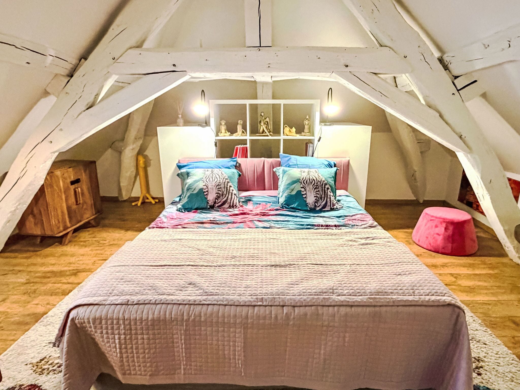 Een gezellig slaapkamer op zolder met een groot bed, een houten garderobe en een plank met decoratieve objecten.