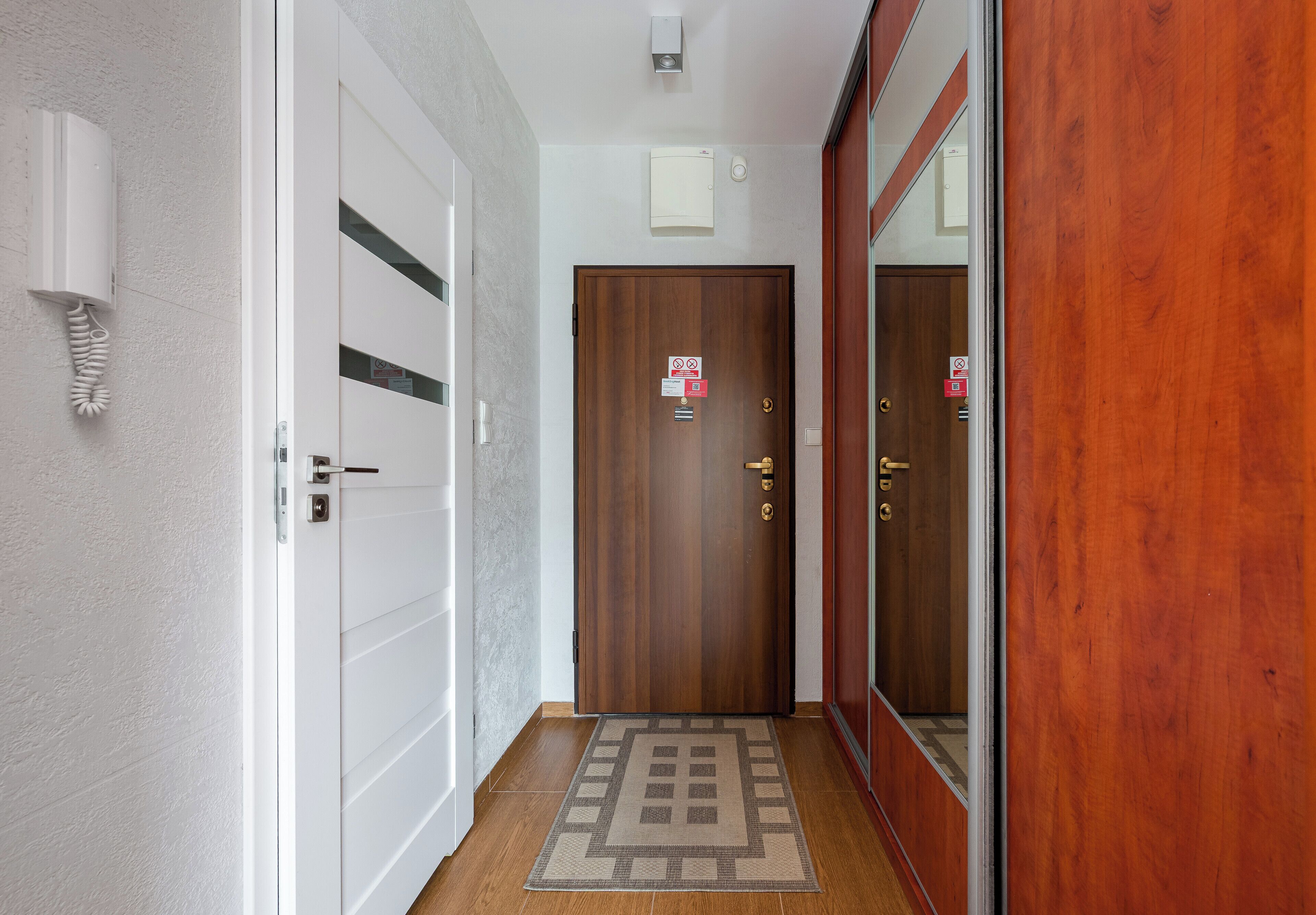 A hallway with a wooden door, a white wall with a telephone, and a patterned rug.