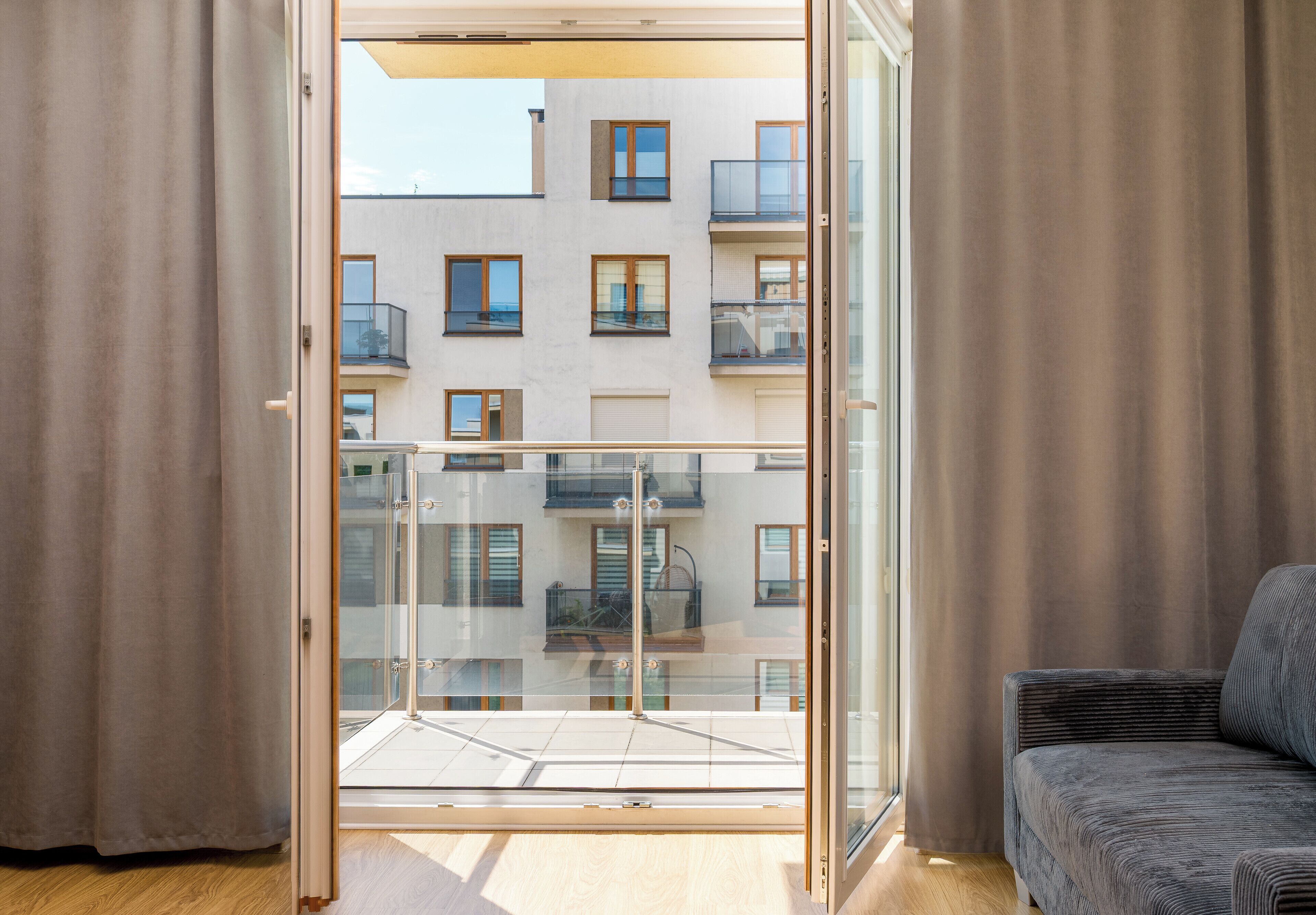 A modern apartment with a balcony, a sofa, and a view of a building with multiple windows.