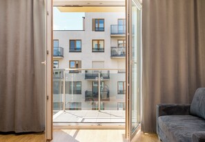 Un apartamento moderno con balcón, un sofá y vista a un edificio con amplias ventanas.