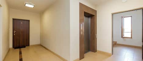 Un pasillo con puerta de madera, un ascensor y una ventana.