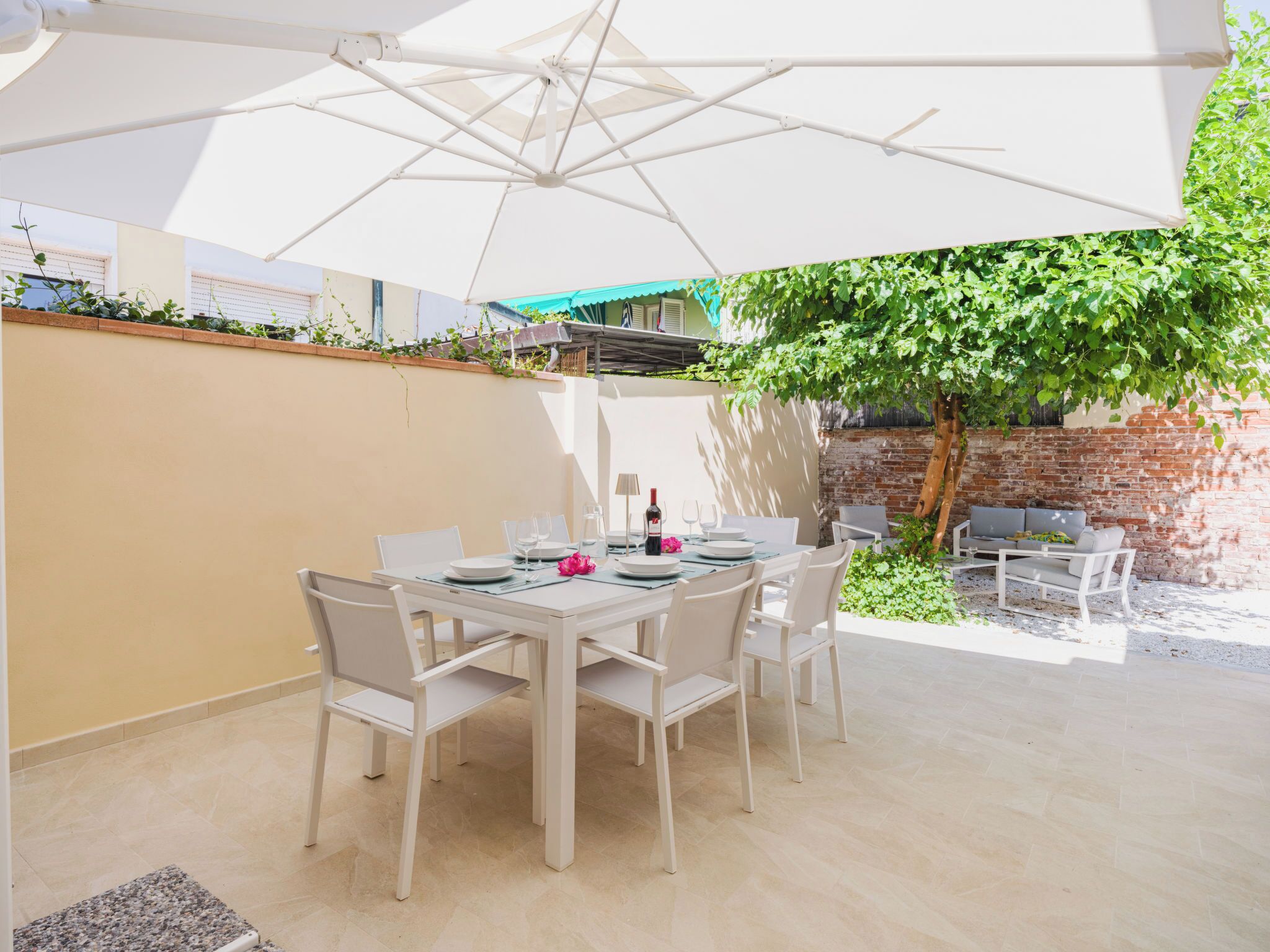 A patio with a table set for dining, surrounded by chairs, under a large umbrella.