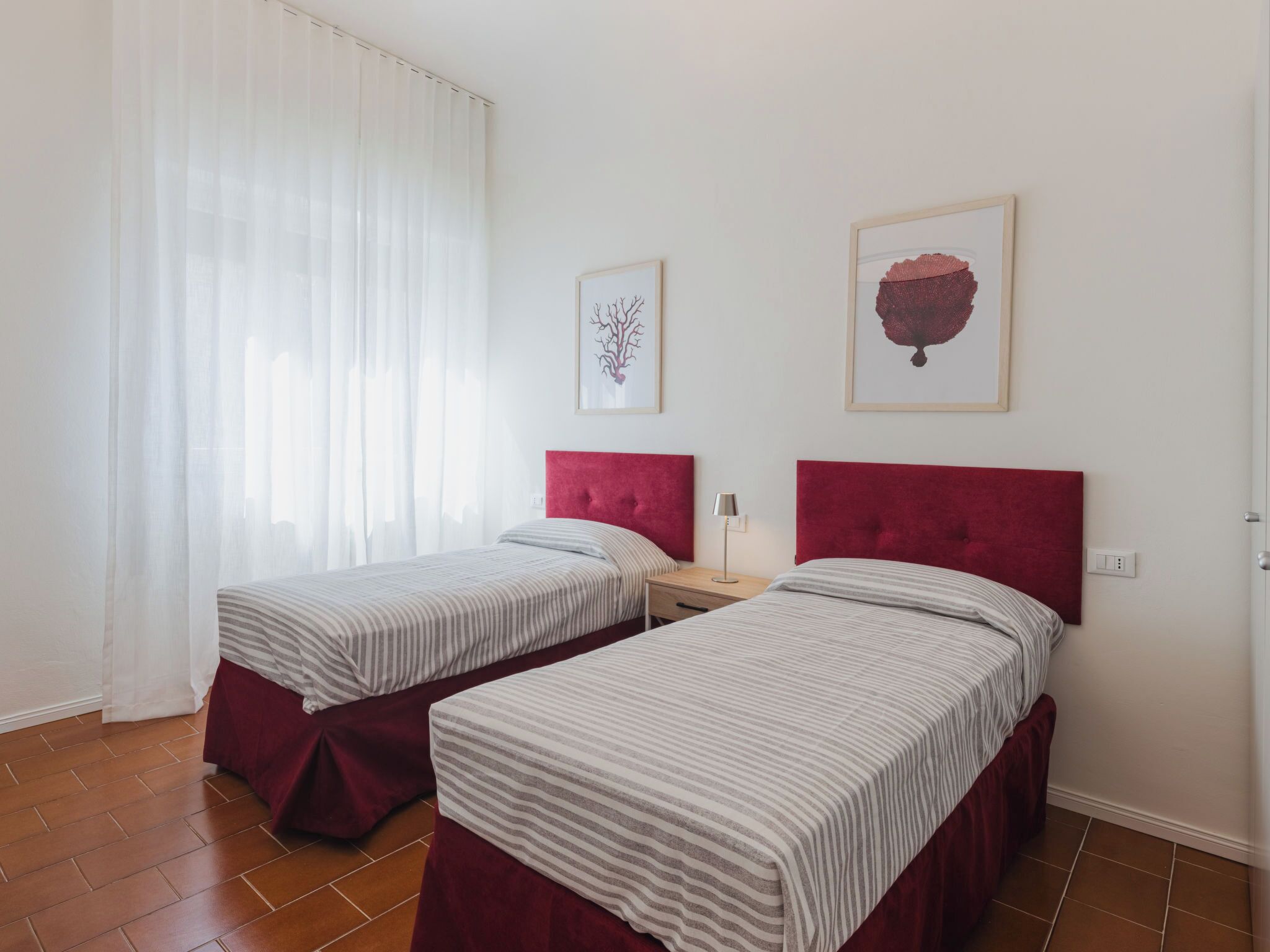 A room with two beds, each with a red headboard, a bedside table with a lamp, and two framed artworks on the wall.