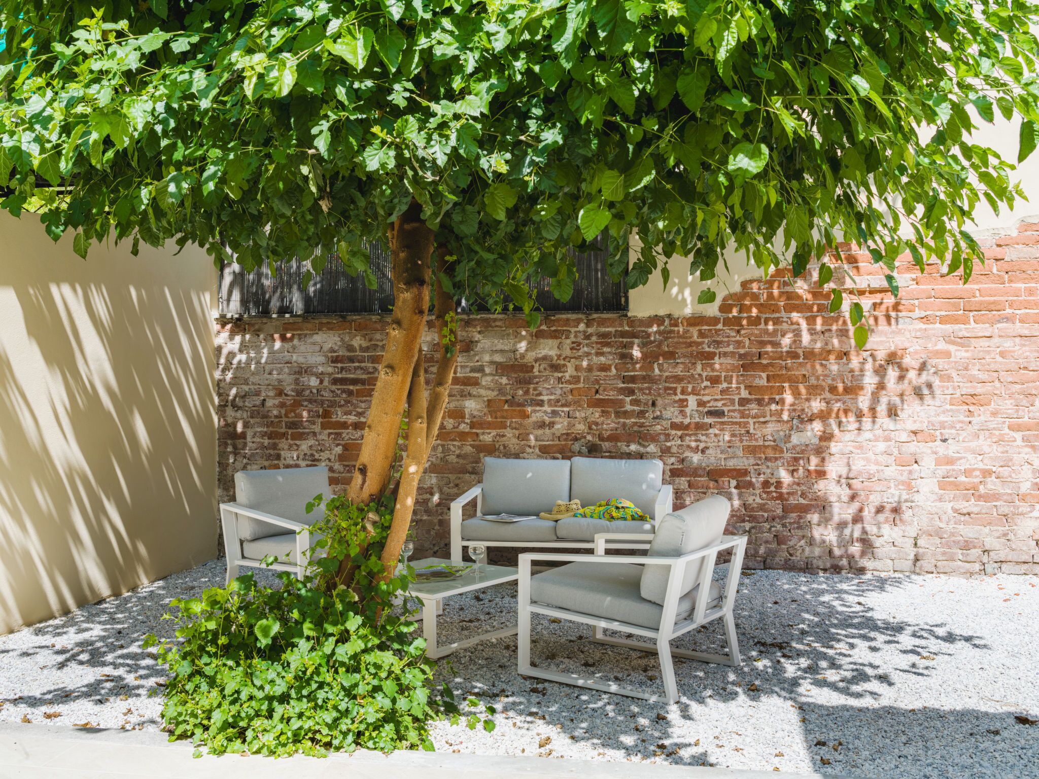 Eine Terrasse mit Backsteinmauer, einem Baum und Gartenmöbeln.