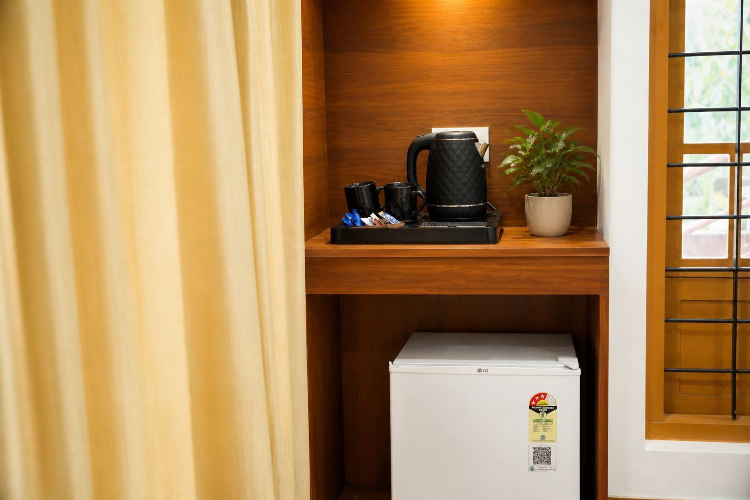 A compact kitchenette with a coffee maker, a small refrigerator, and a potted plant.