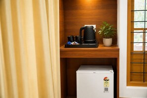 A compact kitchenette with a coffee maker, a small refrigerator, and a potted plant.